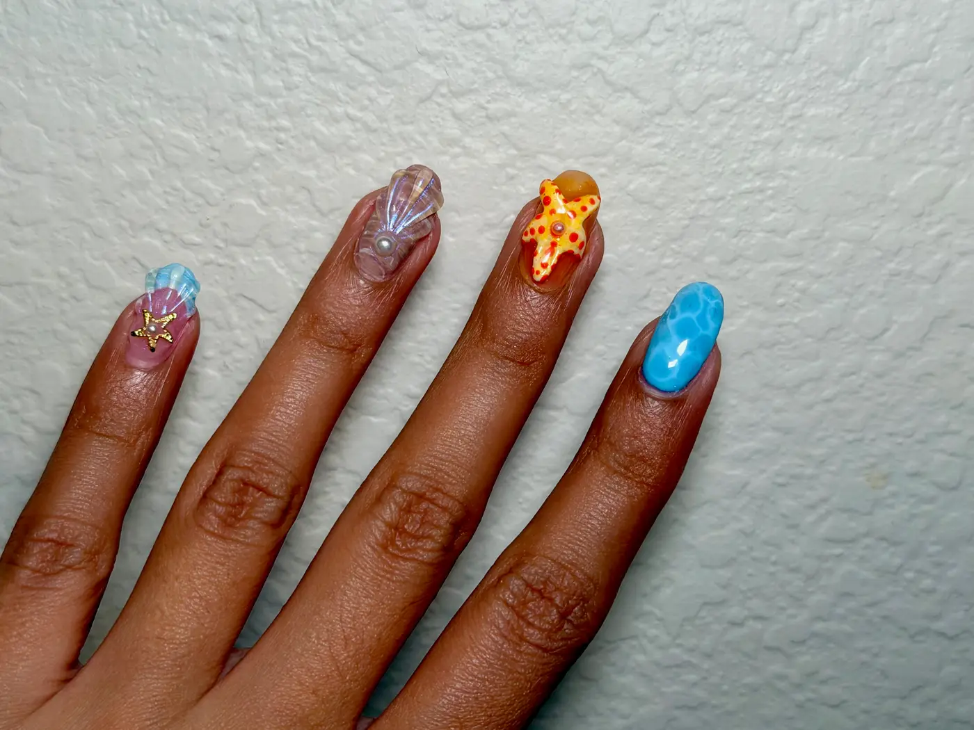 Detail of the ocean set — shell, starfish, and water marbling across four nails